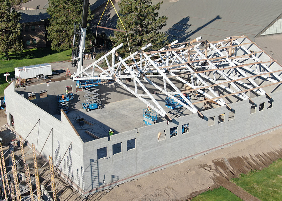 A large crane carefully places one of several a-frame trusses into place with near-impossible accuracy